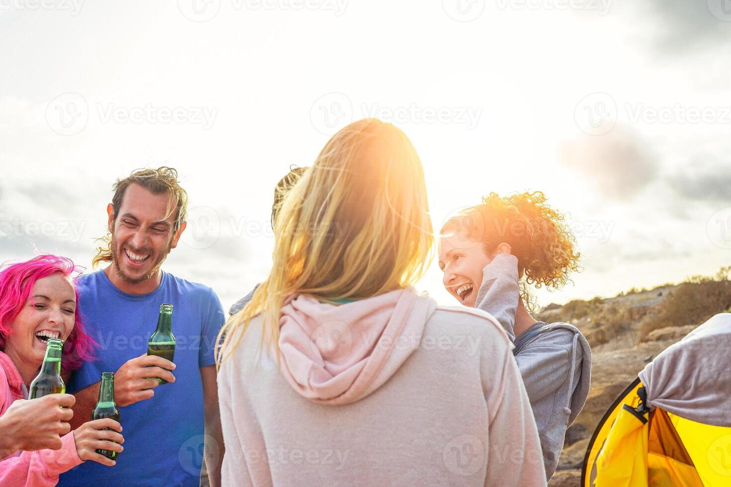 Happy friends drinking beers and having fun camping with tent outdoor - Group of young people enjoying and laughing together in vacation - Travel and youth holidays lifestyle concept photo