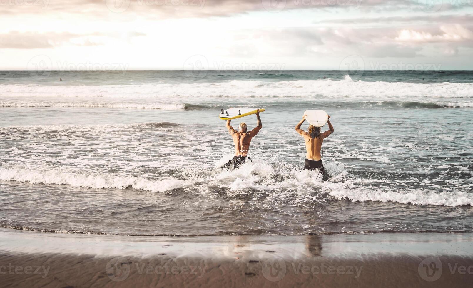 Happy fit friends having fun surfing on sunset time - People doing training exercises in school surfers - Sporty healthy lifestyle and extreme sport concept photo