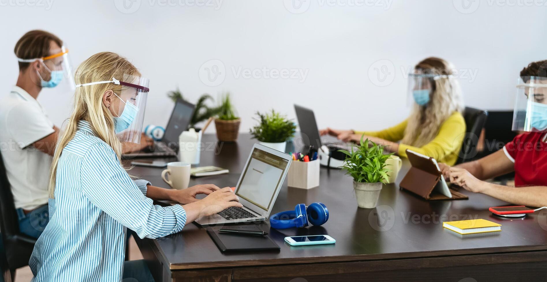 Young people in co-working creative space wearing surgical mask protection for preventing corona virus spread - Millennial friends working with ppe equipment - Social distancing and technology concept photo