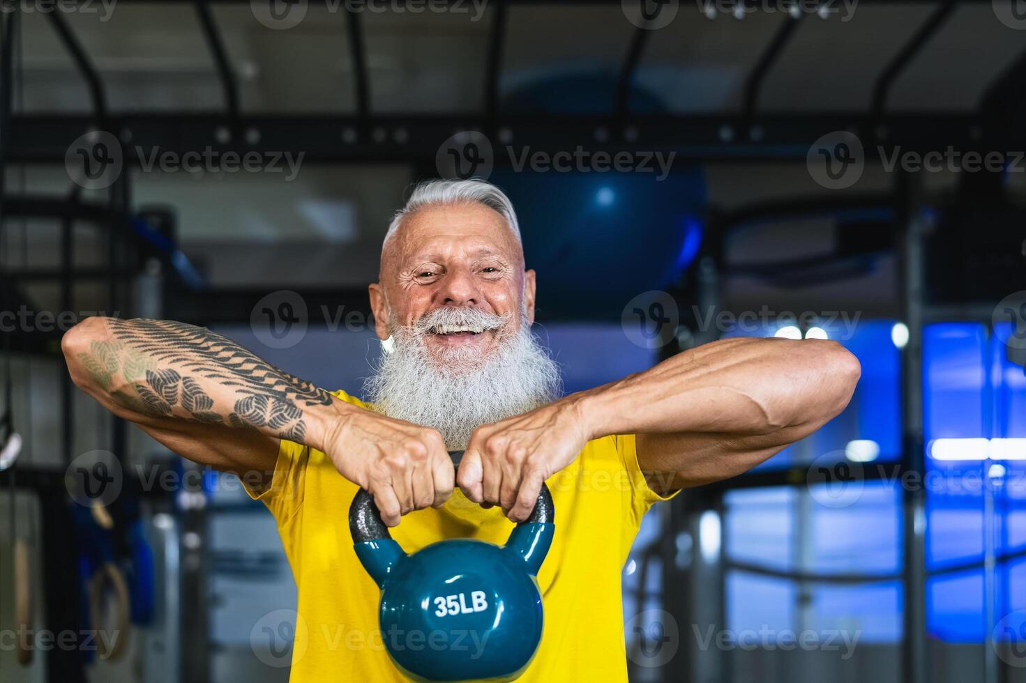 Senior fitness man doing kettle bell exercises inside gym - Fit mature male training in wellness club center - Body building and sport healthy lifestyle concept photo