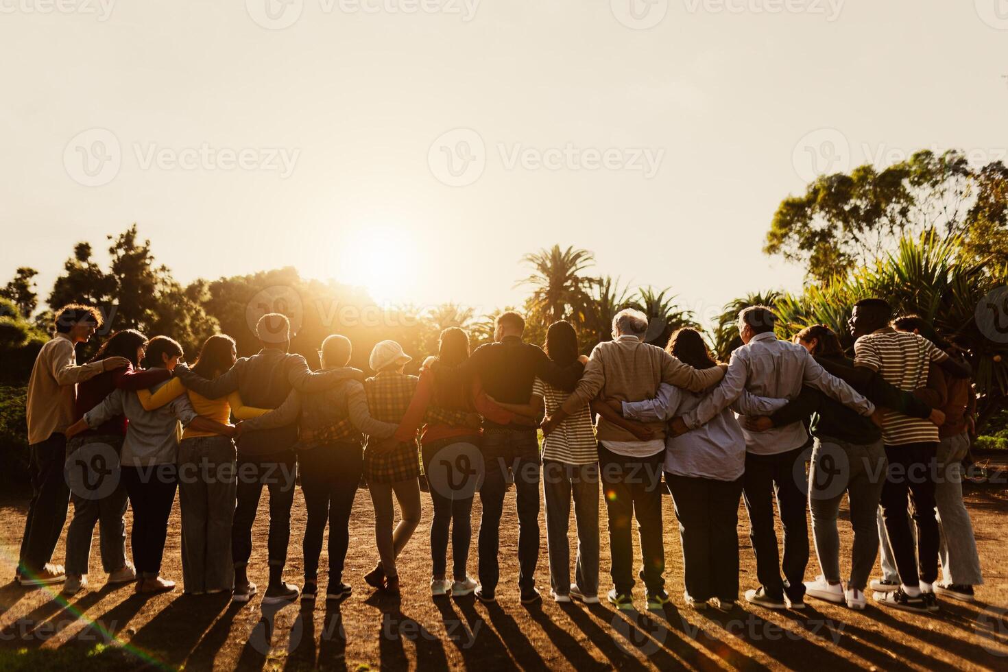 espalda ver de contento multigeneracional personas teniendo divertido en un público parque durante puesta de sol hora - comunidad y apoyo concepto foto