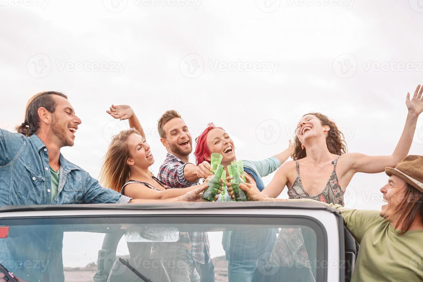 Happy friends having fun drinking champagne on convertible offroad car - Young crazy people making party during vacation - Travel people and youth holidays culture lifestyle concept photo