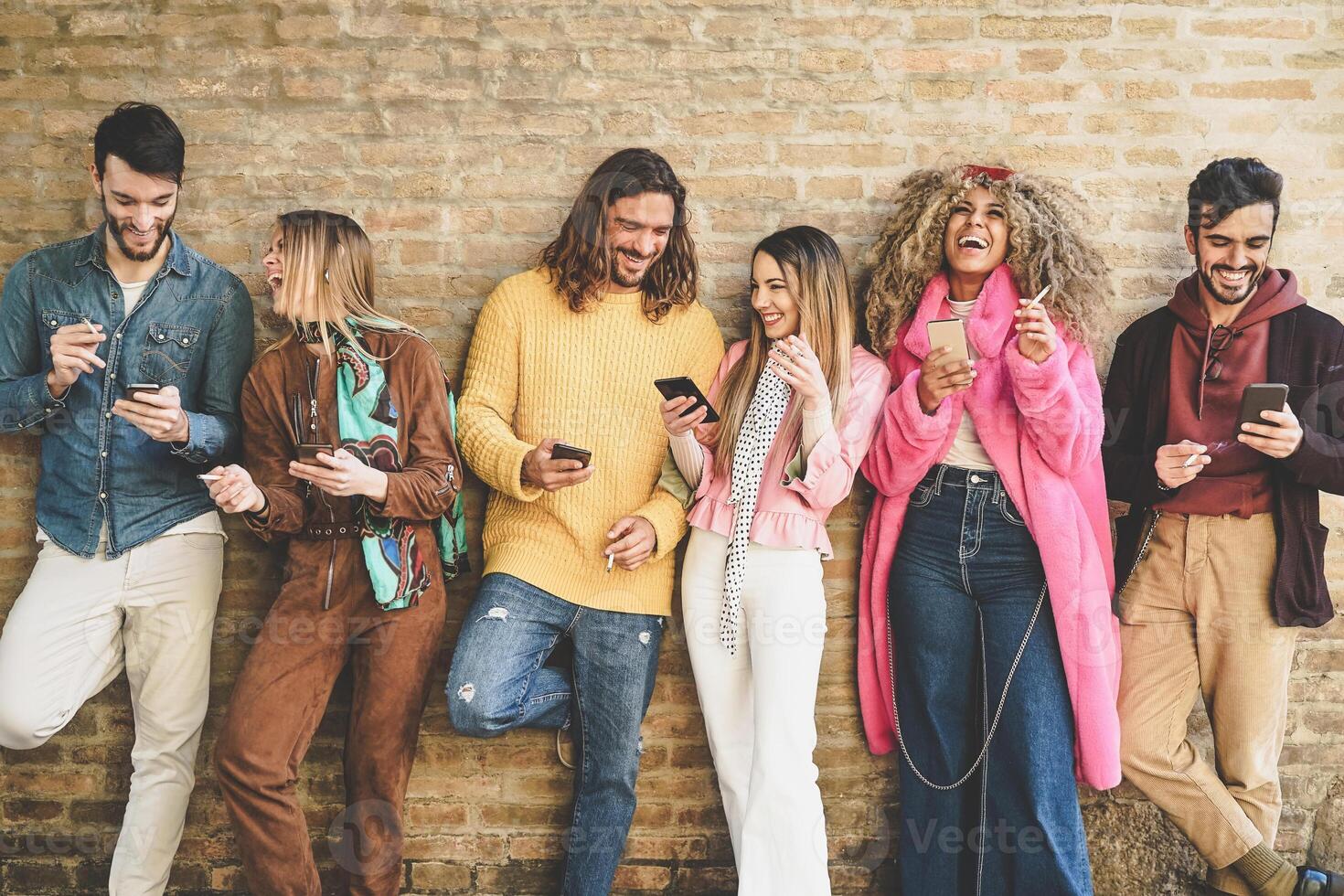 Group of friends using mobile phones outdoor - Young happy people having fun with smartphone apps while smoking cigarettes in the city center - Addiction, tech and youth lifestyle concept photo