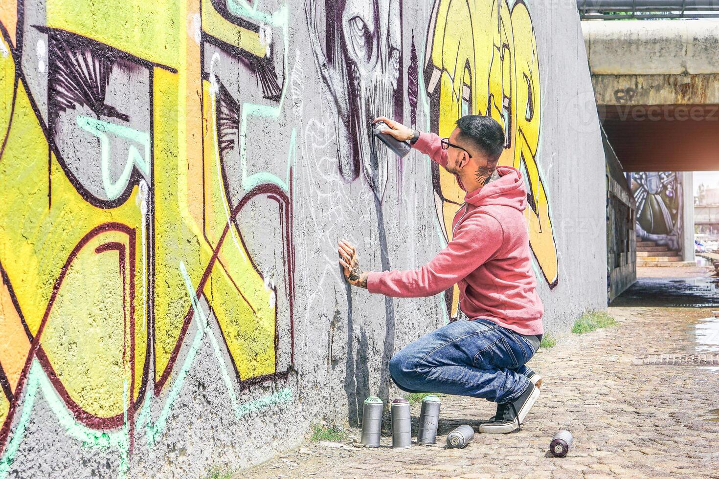 Street graffiti artist painting with a color spray can a dark monster skull graffiti on the wall in the city outdoor - Urban, lifestyle contemporary street art concept - Main focus on his hand photo