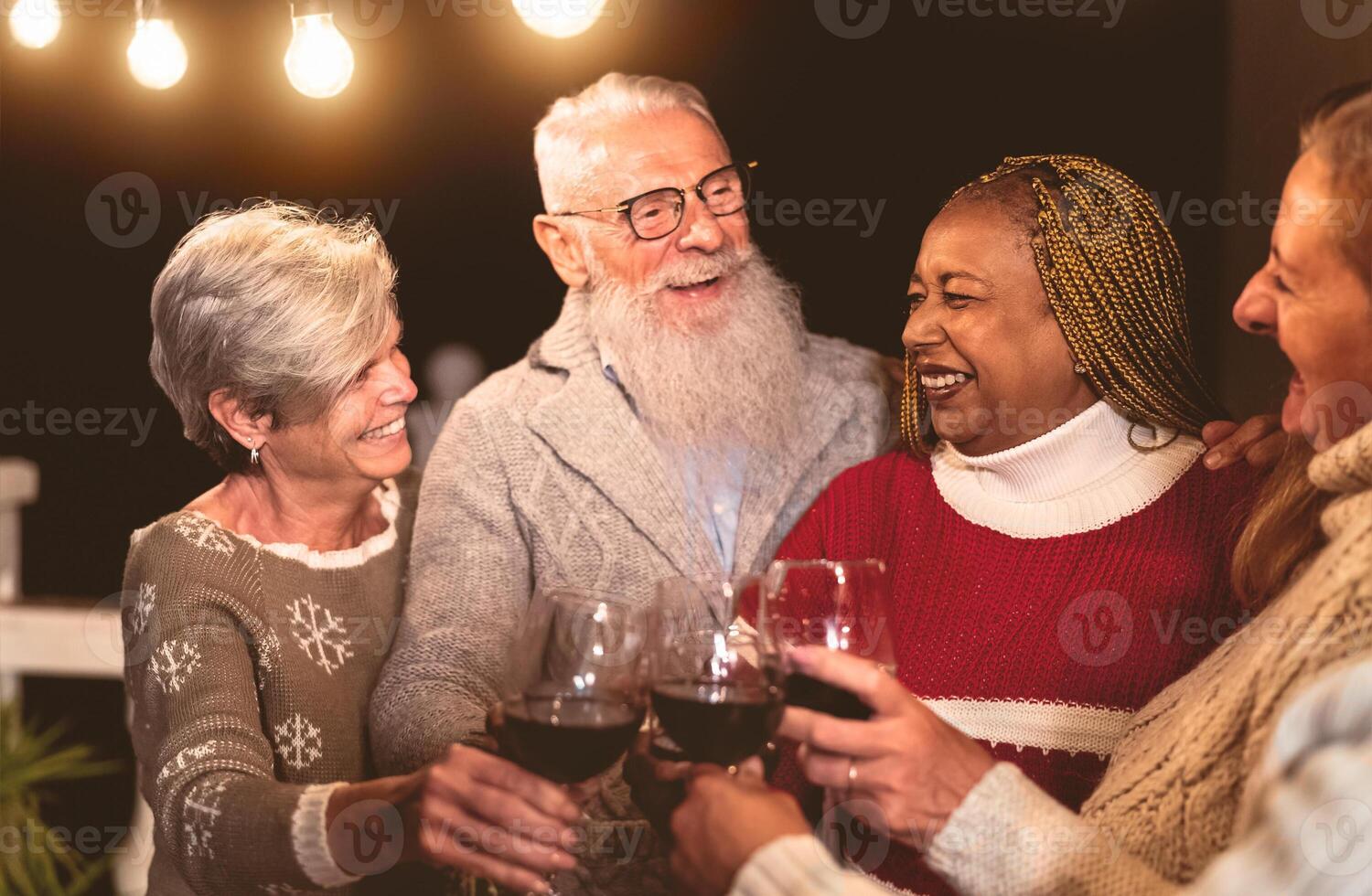 Happy senior friends celebrating holidays while toasting with red wine glasses on house patio party photo