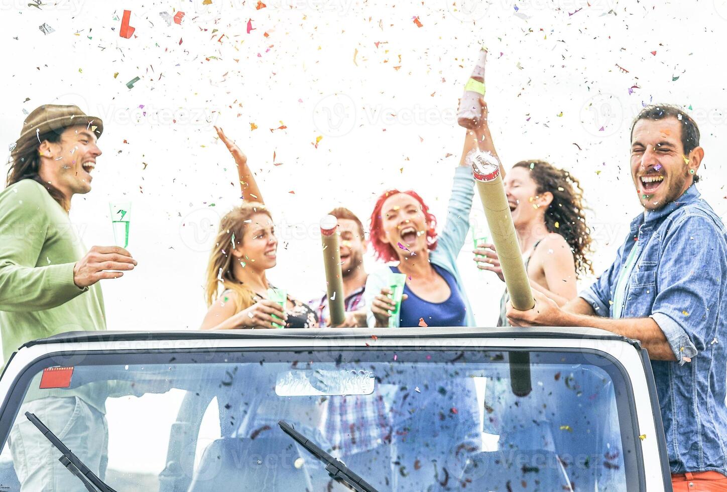 Group of happy friends making party throwing confetti on convertible jeep car - Young people celebrating and having fun drinking champagne and laughing together outdoor - Youth lifestyle concept photo