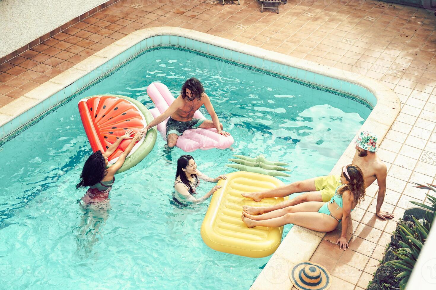Happy friends having fun in swimming pool  during summer vacation - Young people relaxing and floating on air lilos in the pool resort - Friendship, holidays and youth lifestyle concept photo