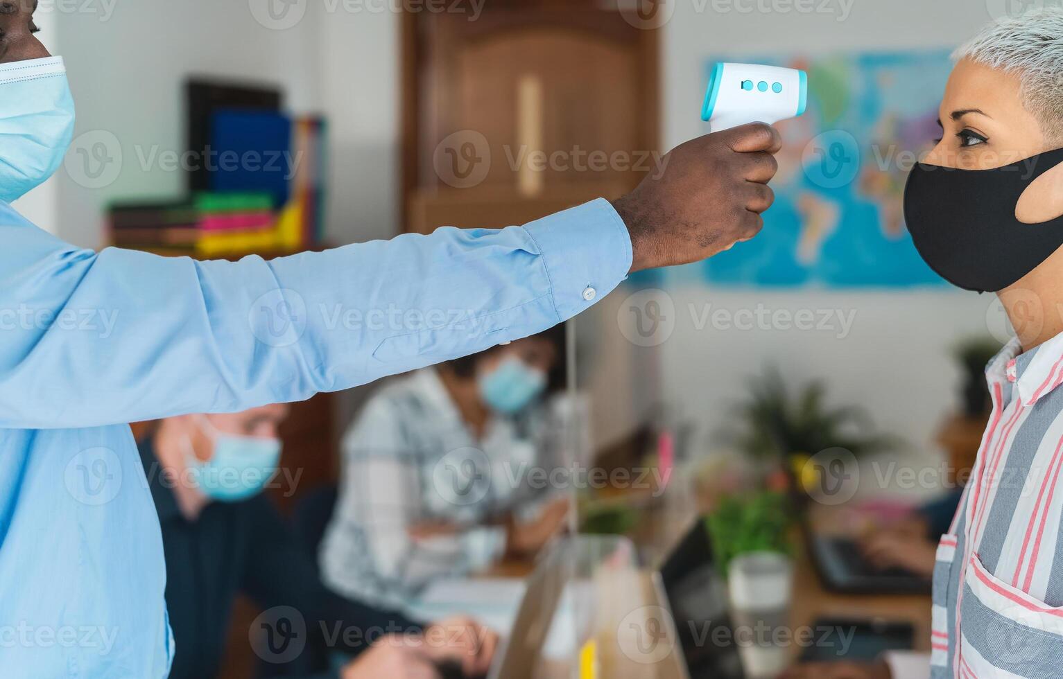 Young people in co-working creative space checkup temperature with digital thermometer while wearing face mask and keeping social distance to avoid corona virus spread photo