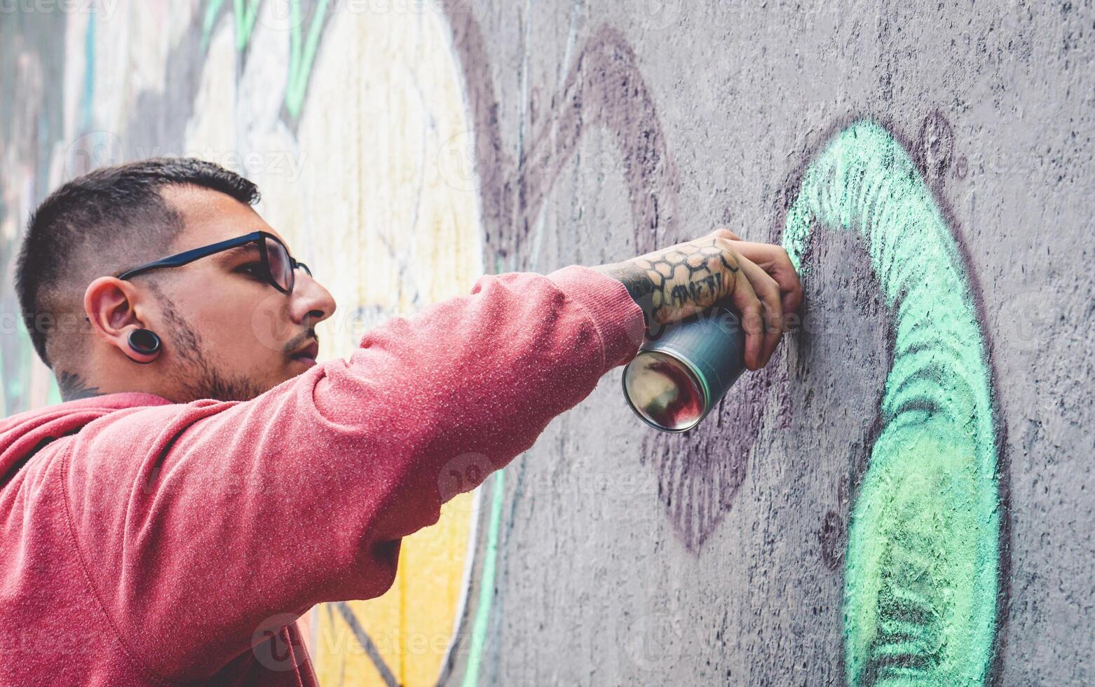 Street graffiti artist painting with a color spray can mural graffiti on the wall in the city - Urban and modern street art lifestyle concept photo