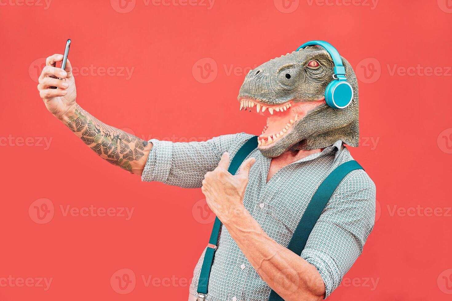 loco mayor hombre vistiendo tirano saurio Rex máscara y tomando selfie con móvil teléfono inteligente - hipster más viejo masculino teniendo divertido escuchando música y bailando al aire libre - absurdo, gracioso y surrealista conceptos foto