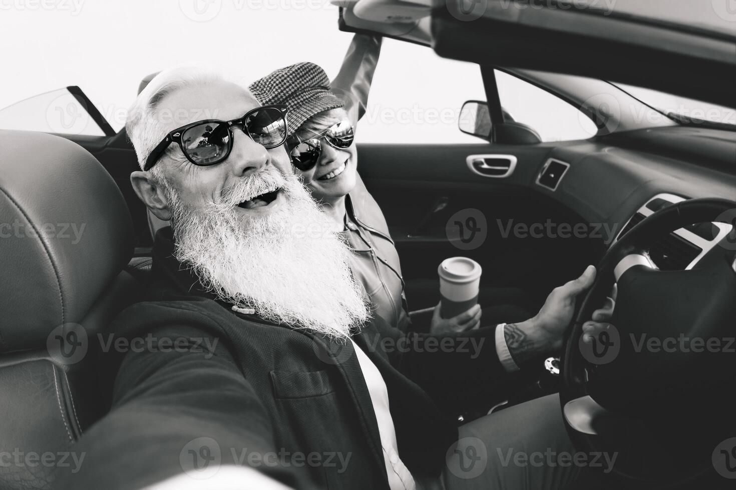 Happy senior couple taking selfie on new convertible car - Mature people having fun together during road trip vacation - Elderly lifestyle and travel transportation concept - Black and white editing photo