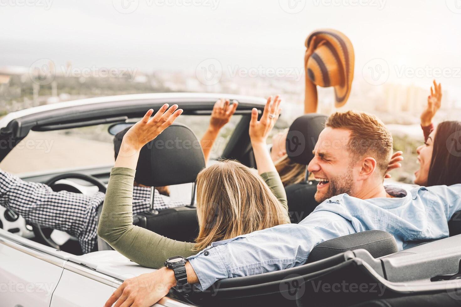 Group of friends having fun in convertible car during road trip at sunset - Young travel people driving a cabriolet during summer holidays - Happiness, vacation and youth lifestyle concept photo