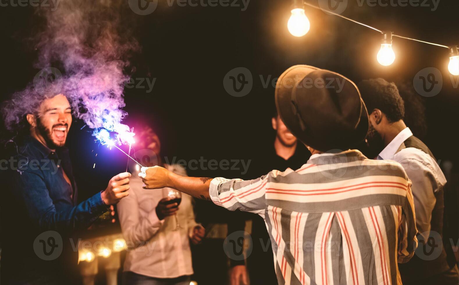 Happy young friends celebrating new year eve with sparklers fireworks and drinking wine on home terrace - Youth people lifestyle and holidays concept photo