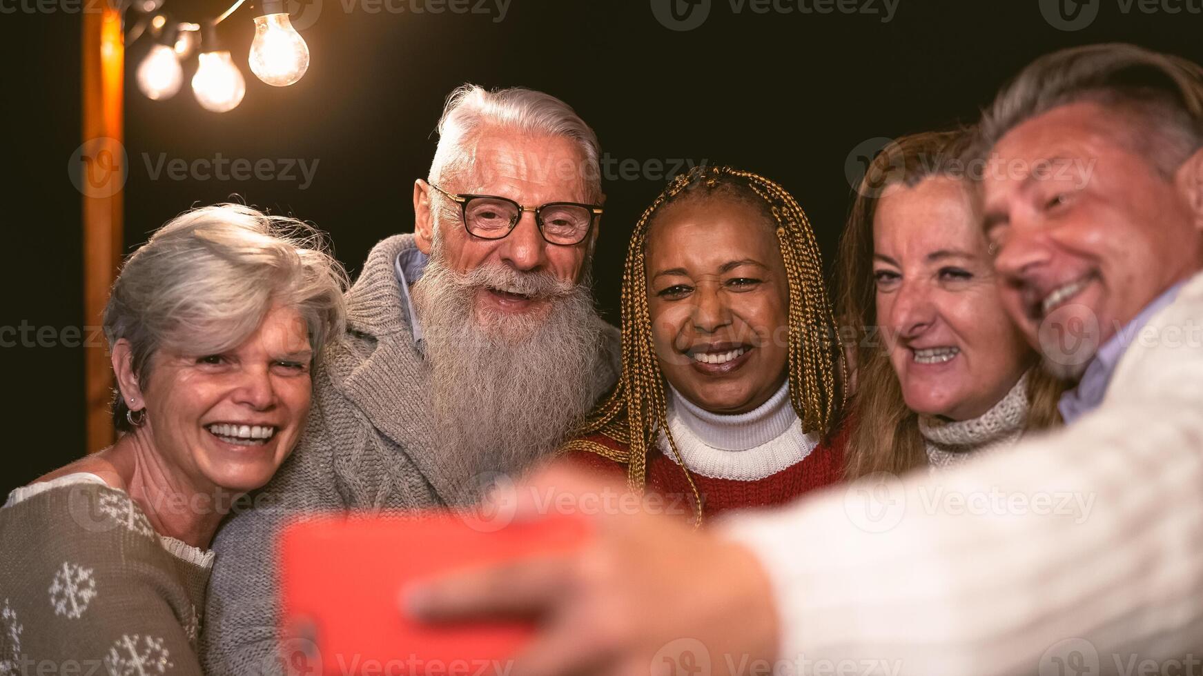 Happy multiracial senior friends having fun in holidays taking selfie with mobile smartphone on house patio - Elderly lifestyle people concept photo