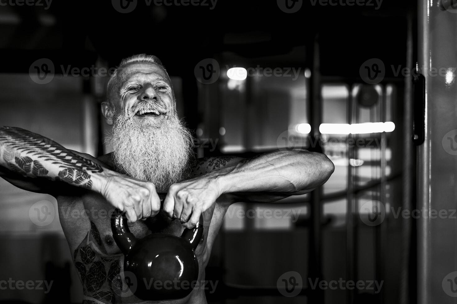 Senior fitness man doing kettle bell exercises inside gym - Fit mature male training in wellness club center - Body building and sport healthy lifestyle concept - Black and white editing photo