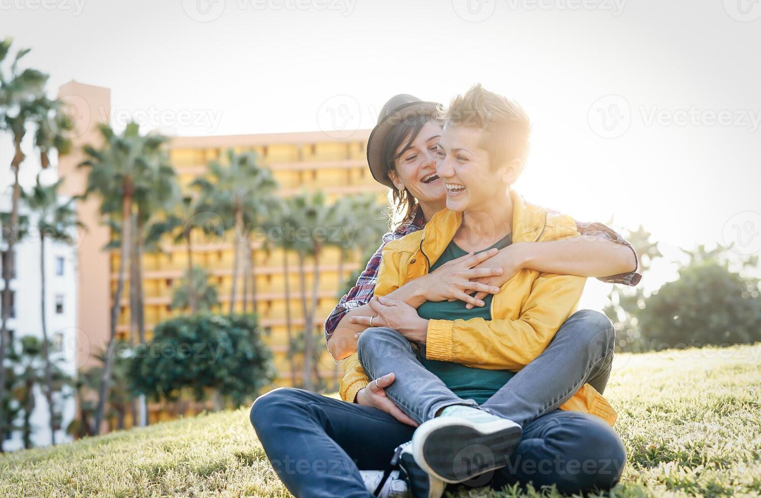 contento gay Pareja en un romántico fecha abrazando y riendo juntos sentado en césped en un parque - joven lesbianas teniendo un oferta momento al aire libre - lesbianas, bisexualidad, relación estilo de vida concepto foto