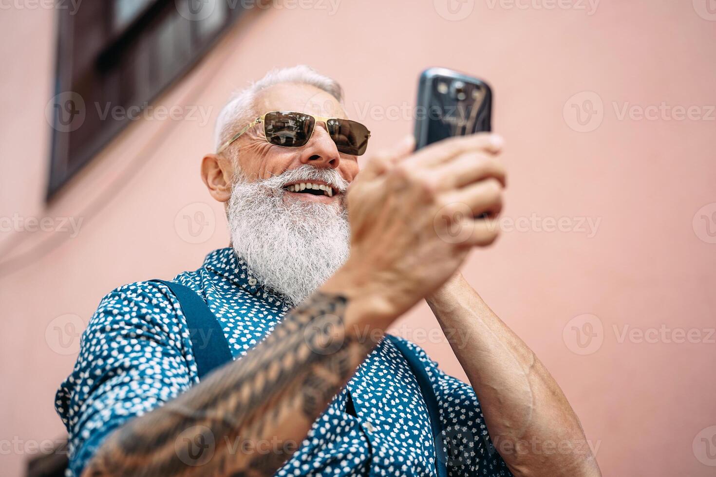 Happy senior man messaging on mobile smartphone outdoor - Bearded hipster fashion male having fun with new technology apps for social media - Concept of tech and elderly fashion people photo