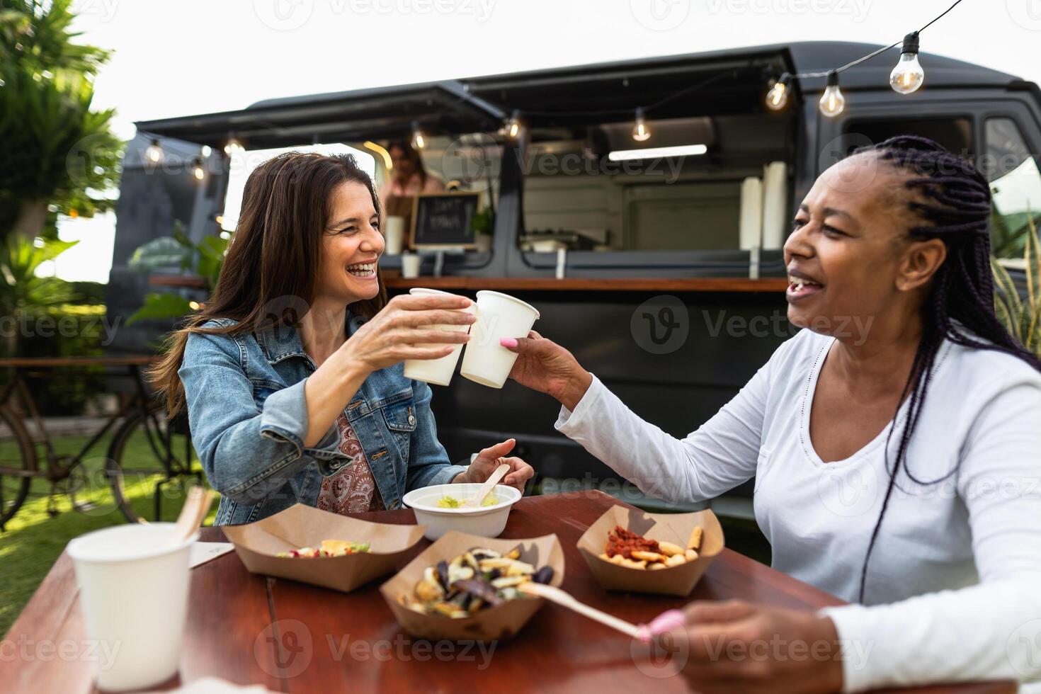 Happy multiracial senior friends having fun eating in a street food truck market photo