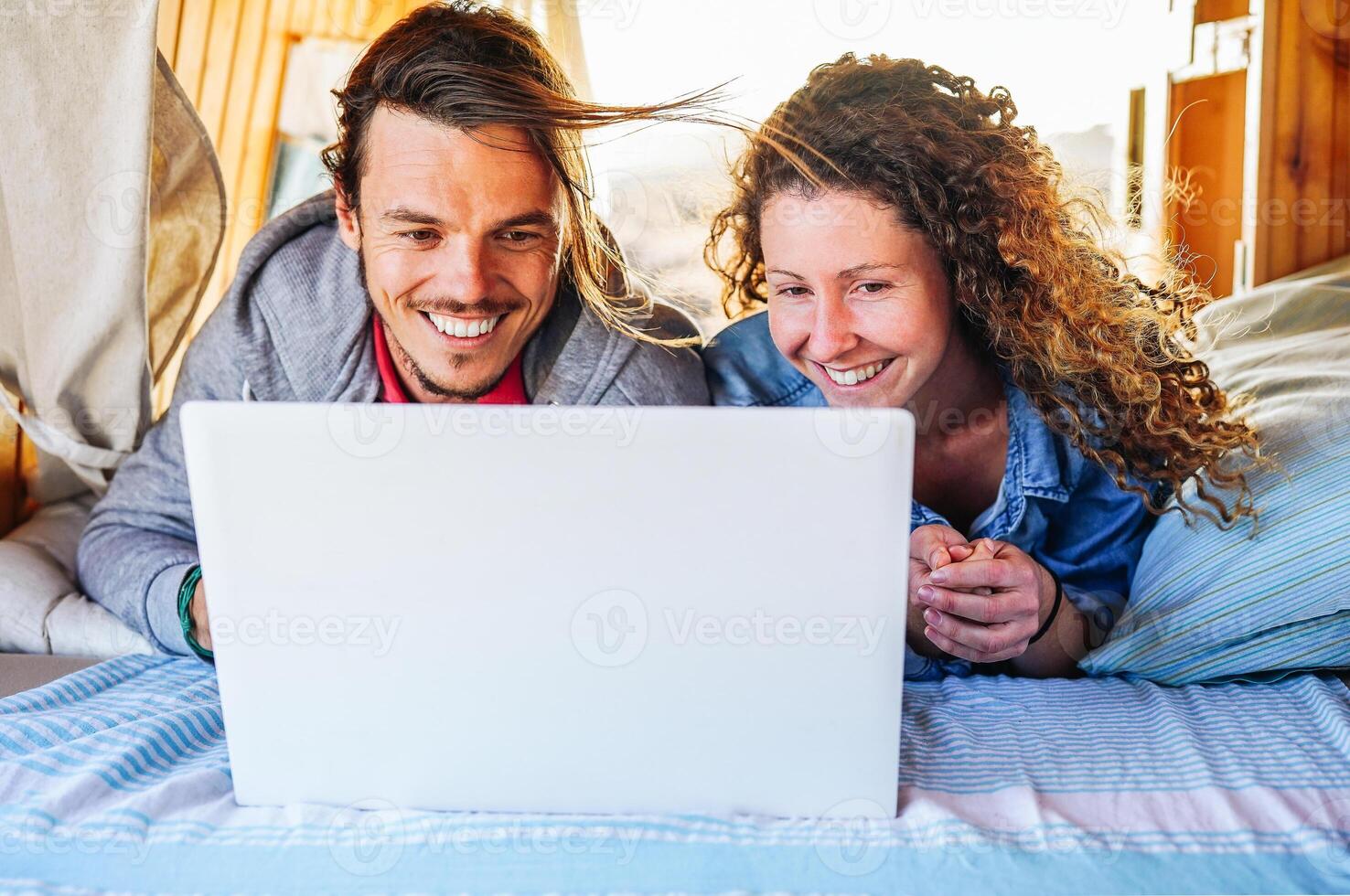 Happy couple watching on their computer on the bed - Travel people using laptop during their journey on a vintage minivan with wood interior - Vacation, love, technology concept photo