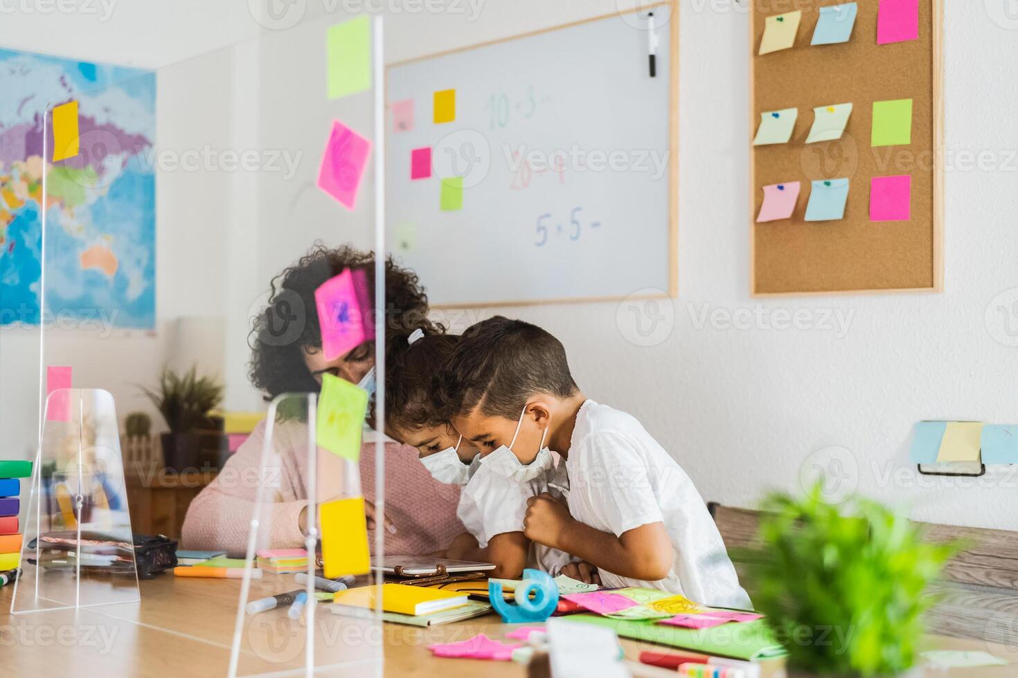 Teacher with children wearing face mask in preschool classroom during corona virus pandemic - Education and safety school measures for preventing covid19 photo