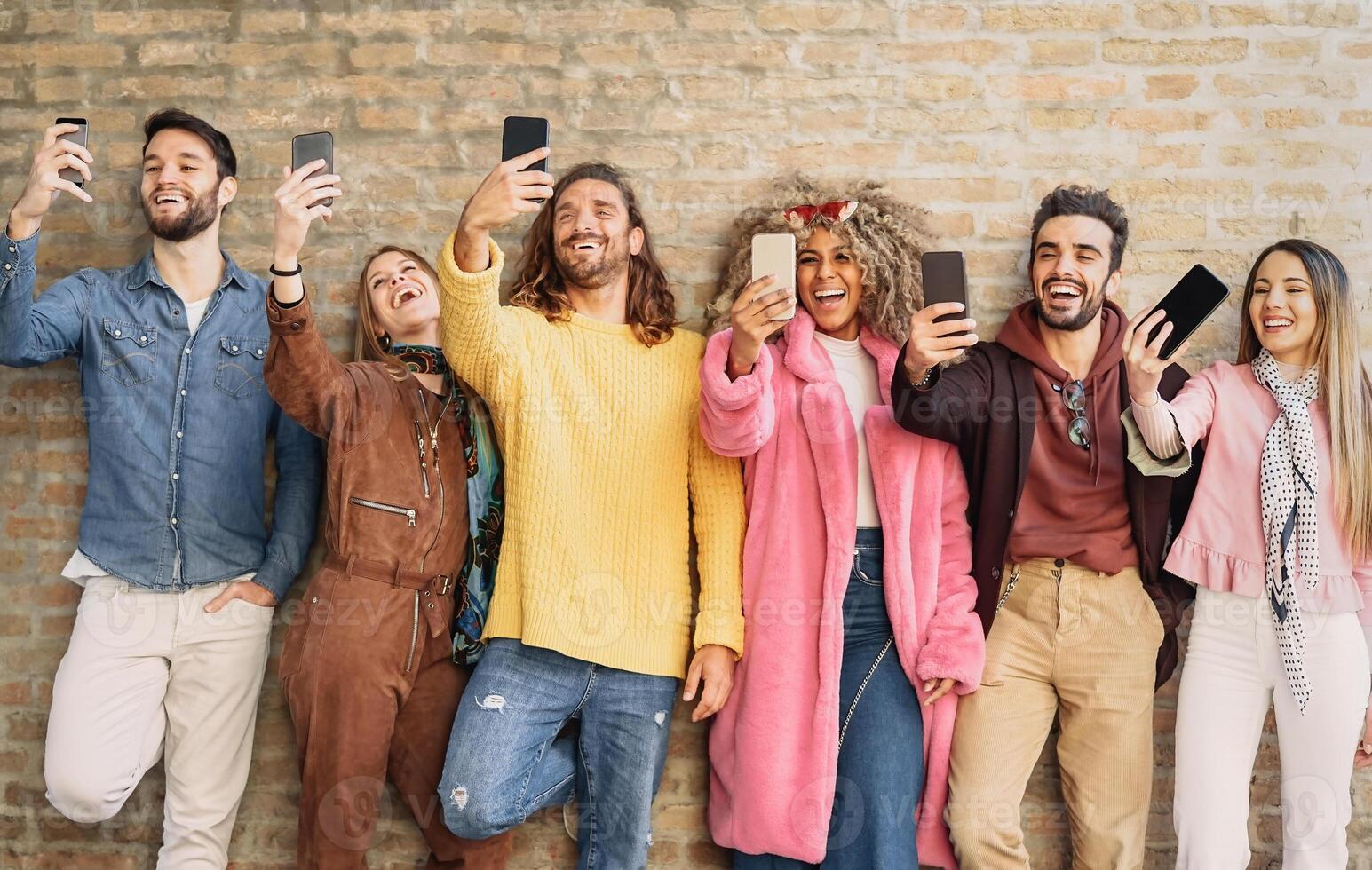 Happy group friends taking selfie with cell phone outdoor - Young trendy people having fun with new mobile smartphone apps for social media - Youth culture millennial generation and Technology concept photo