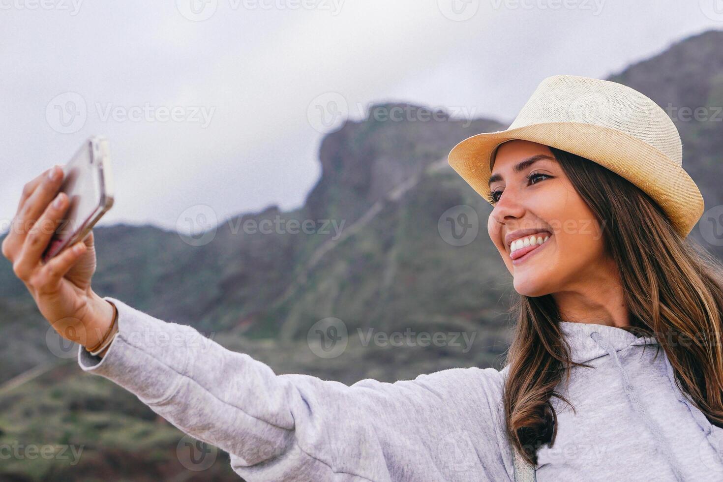 joven hermosa mujer en vacaciones tomando un selfie con su móvil teléfono inteligente cámara con montaña en el antecedentes - teléfono, social, adiccion y viaje concepto foto