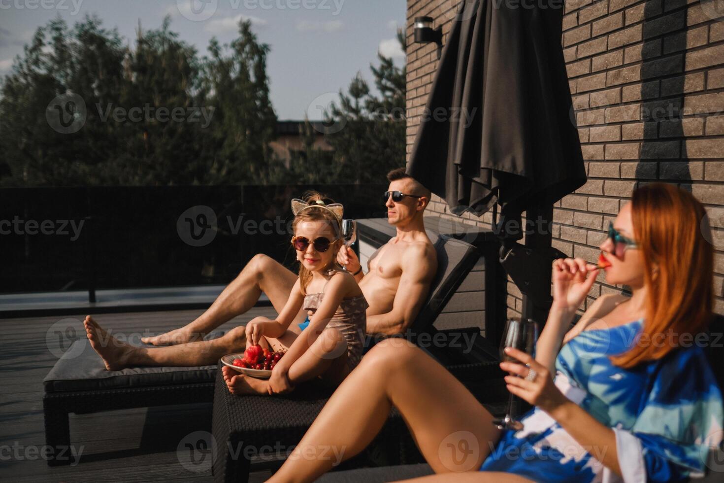 A happy family in swimsuits sunbathe in summer on their terrace on sun beds photo