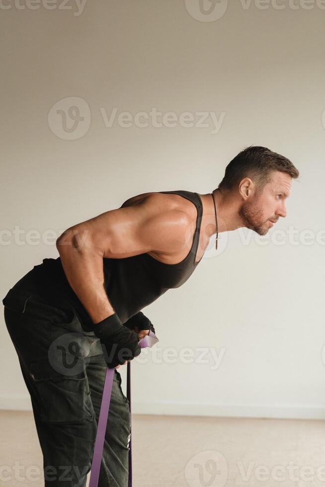 A man in black sportswear is engaged in strength fitness using a rubber loop indoors photo
