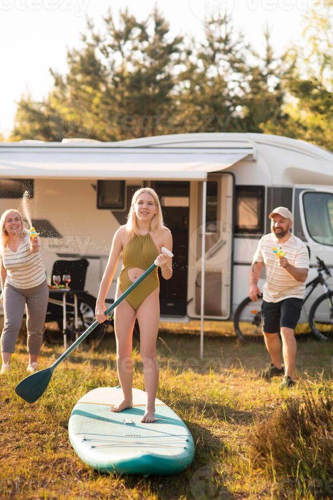 the family is resting next to their mobile home. My daughter is standing with a paddle on a sup board, and her parents pour water on her photo