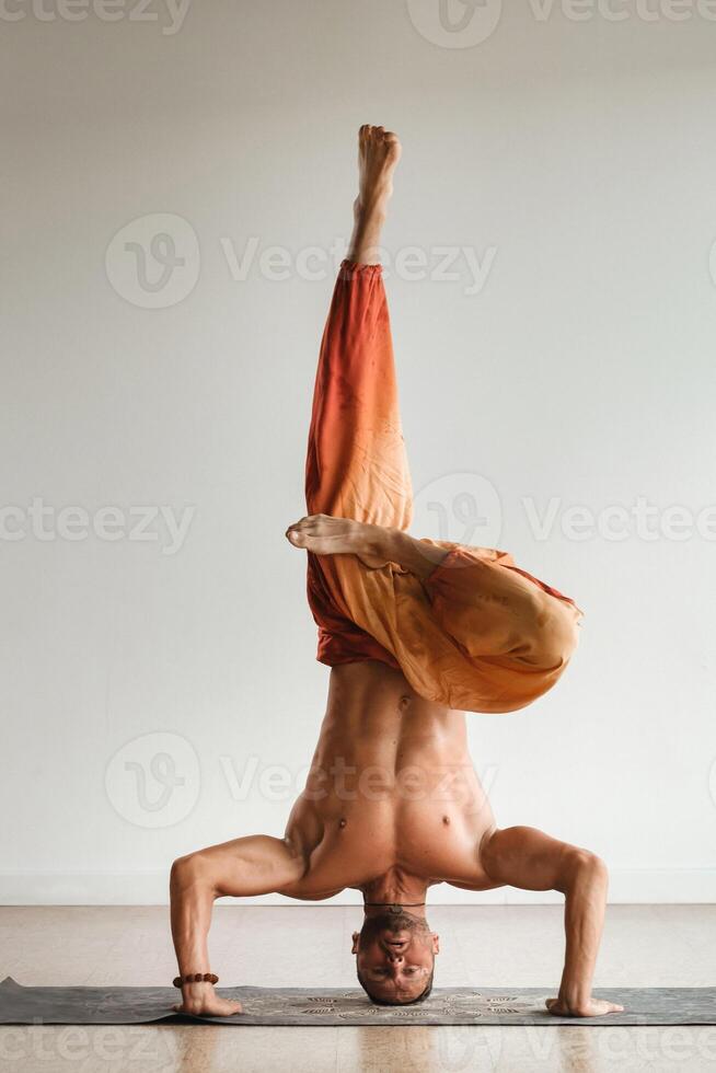 a man with a naked torso does yoga standing on his head indoors. Fitness Trainer photo