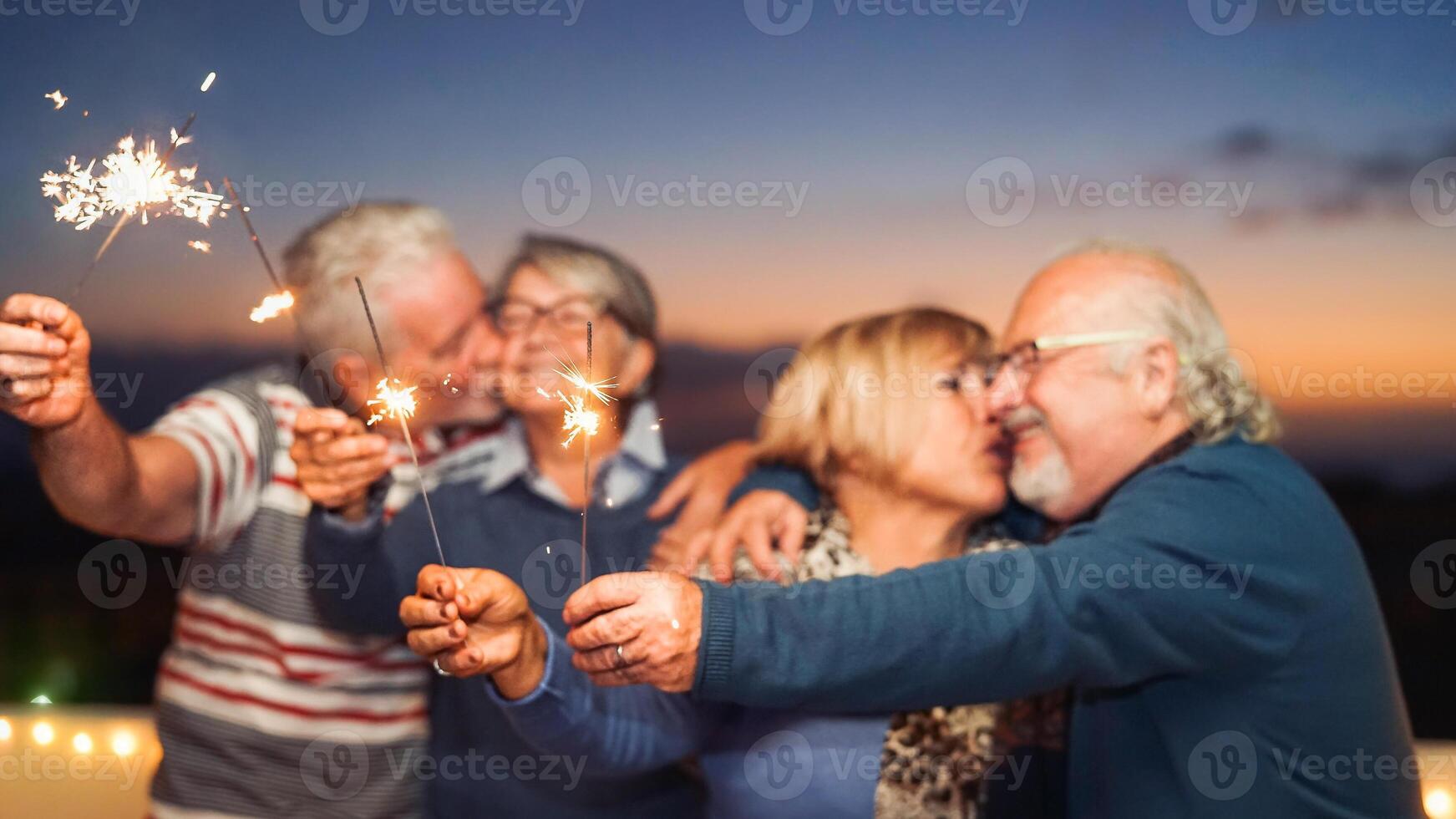 Happy senior friends celebrating with sparklers outdoor - Older people having a fun and tender moment on rooftop - Love, party, elderly lifestyle concept photo