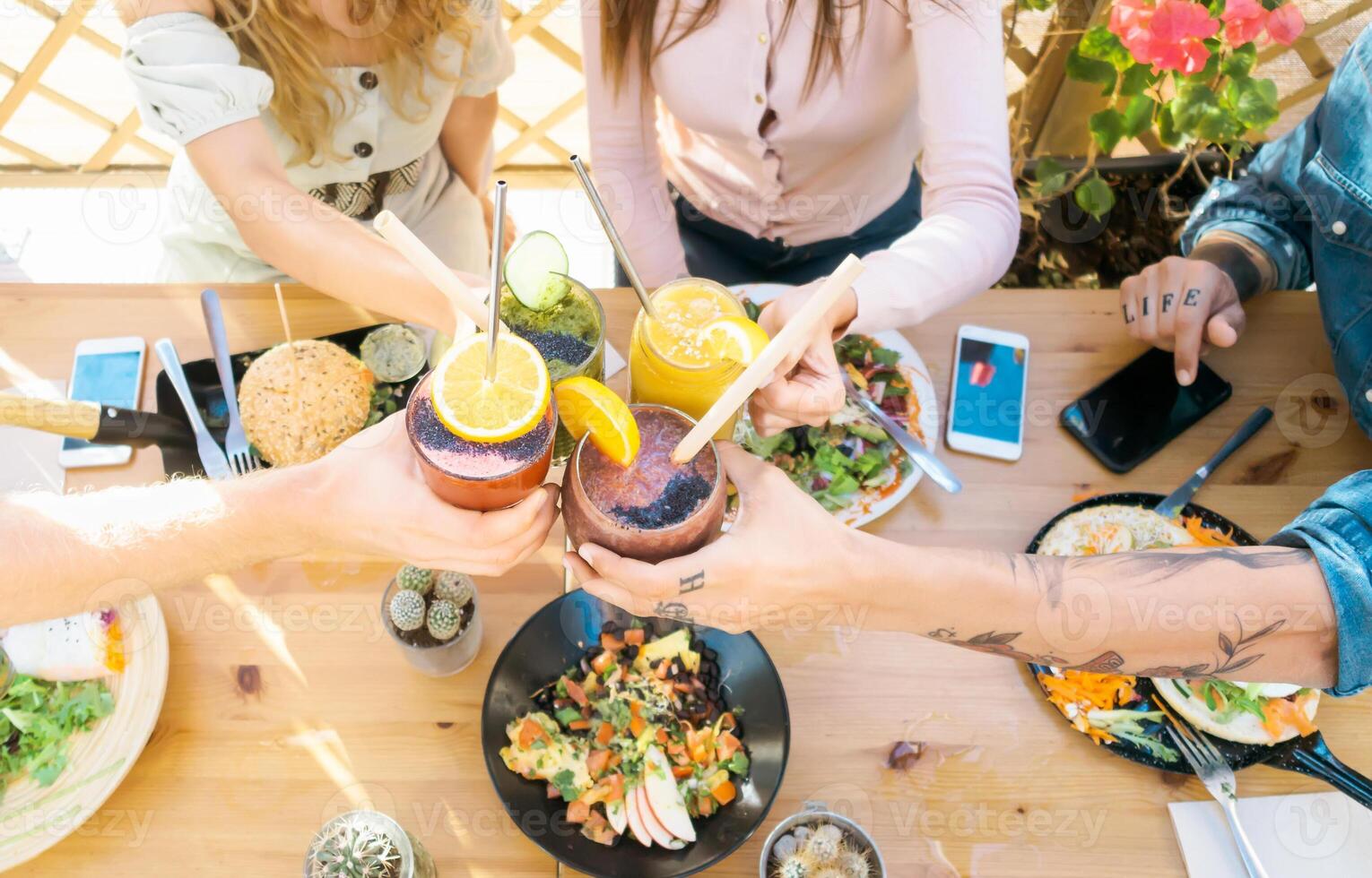 Happy friends cheering with fresh smoothies while lunching together - Young people having fun eating in coffee brunch vintage bar - Healthy food trends and youth lifestyle culture concept photo