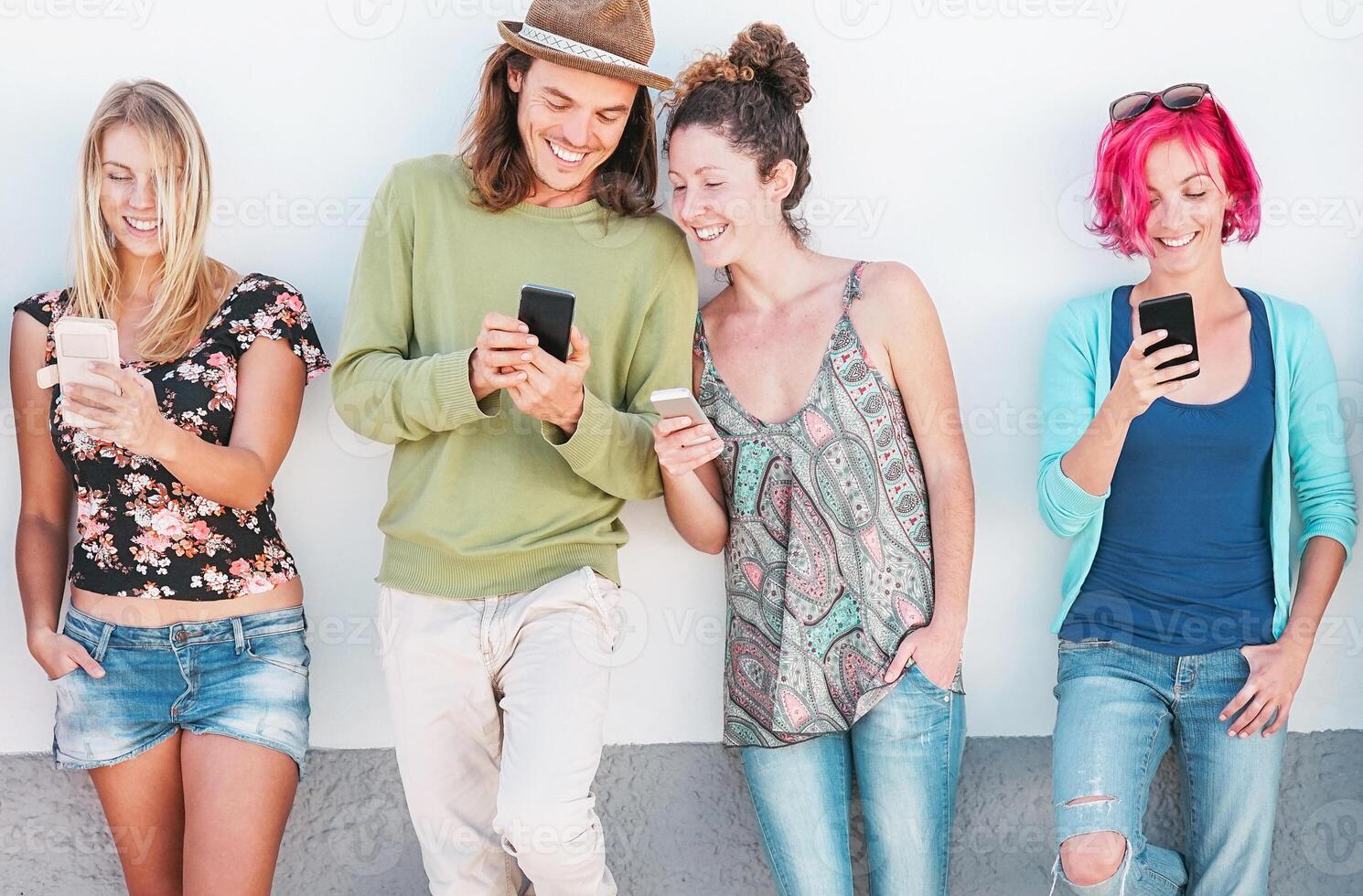 Happy friends watching on their smart mobile phones outdoor - Young generation having fun with new technology and social network - Concept of millennials people, tech and youth addiction lifestyle photo