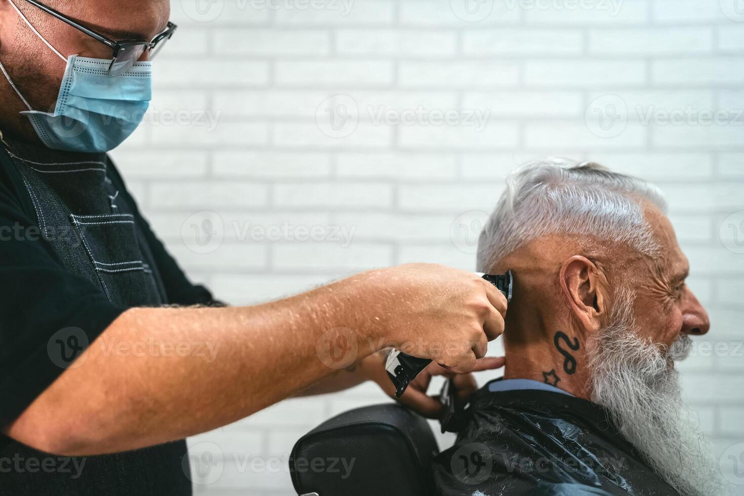 Male hairdresser cutting hair to hipster senior client while wearing face surgical mask - Young hairstylist working in barbershop during corona virus outbreak - Health care and haircut salon concept photo