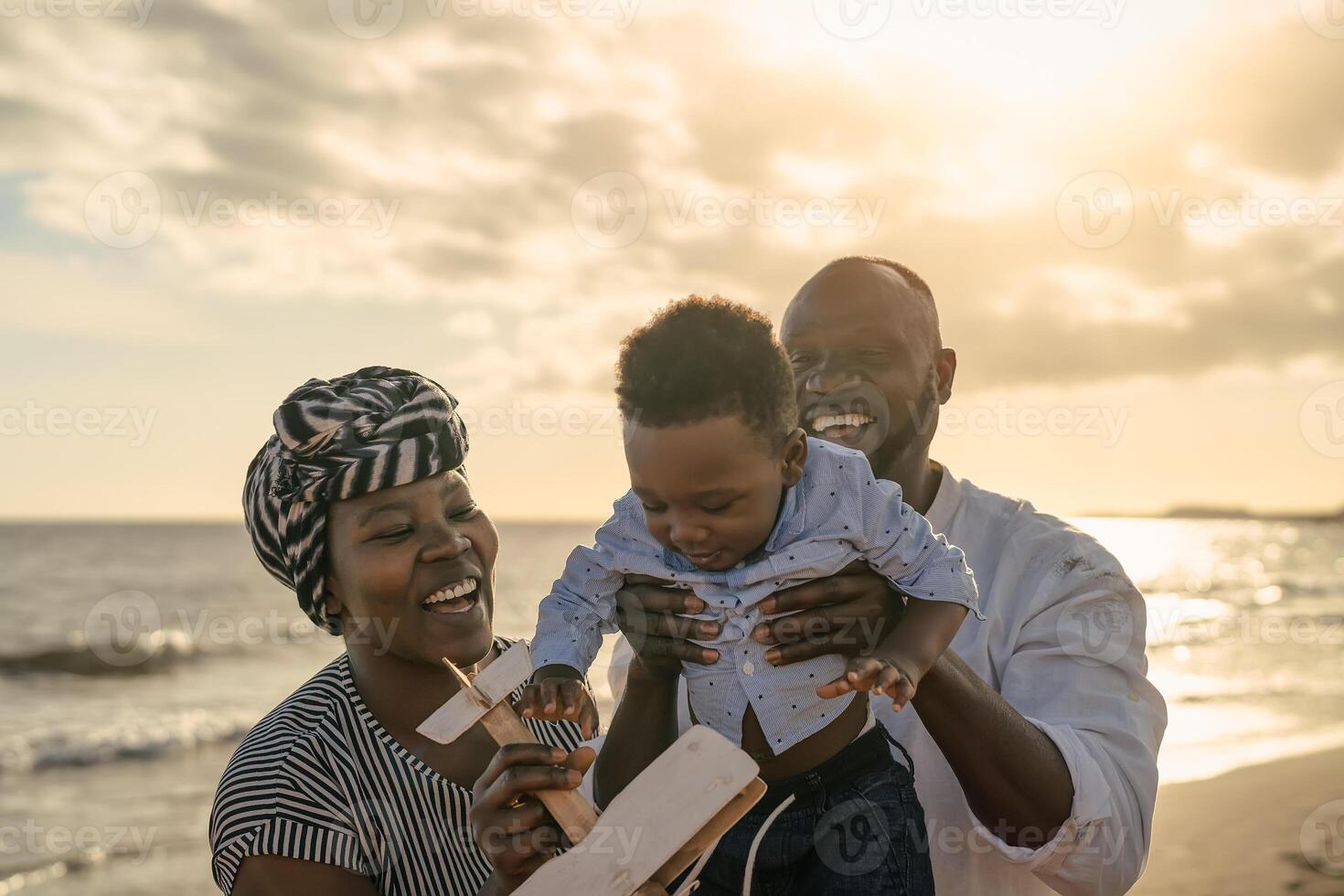 Happy African family having fun on the beach during summer vacation - Parents love and unity concept photo