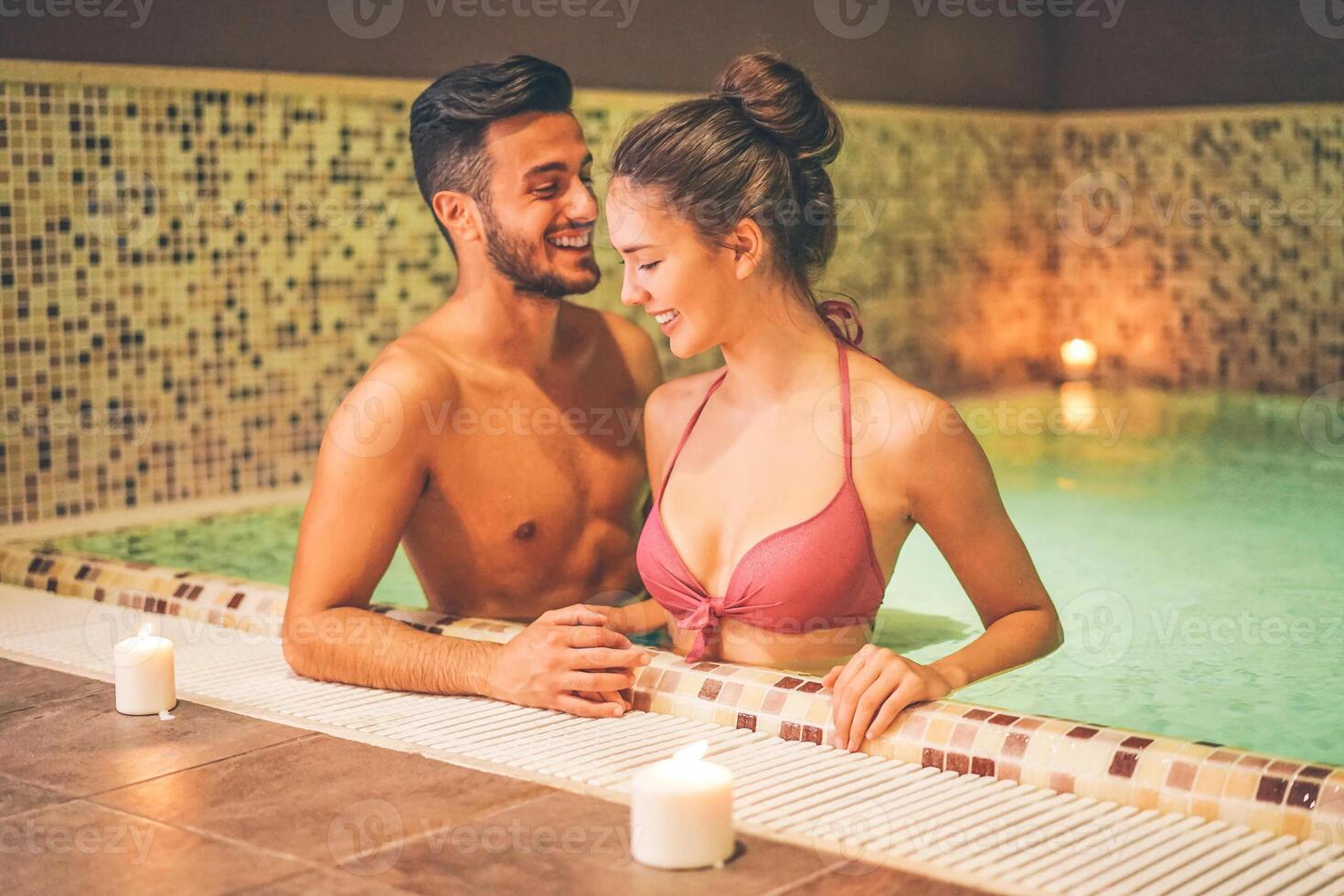 Happy couple relaxing in a warm pool hydro massage at hotel spa. Young lovers having fun in a thermal bath. Couple and well being concept. Soft saturated editing. Focus on female face photo