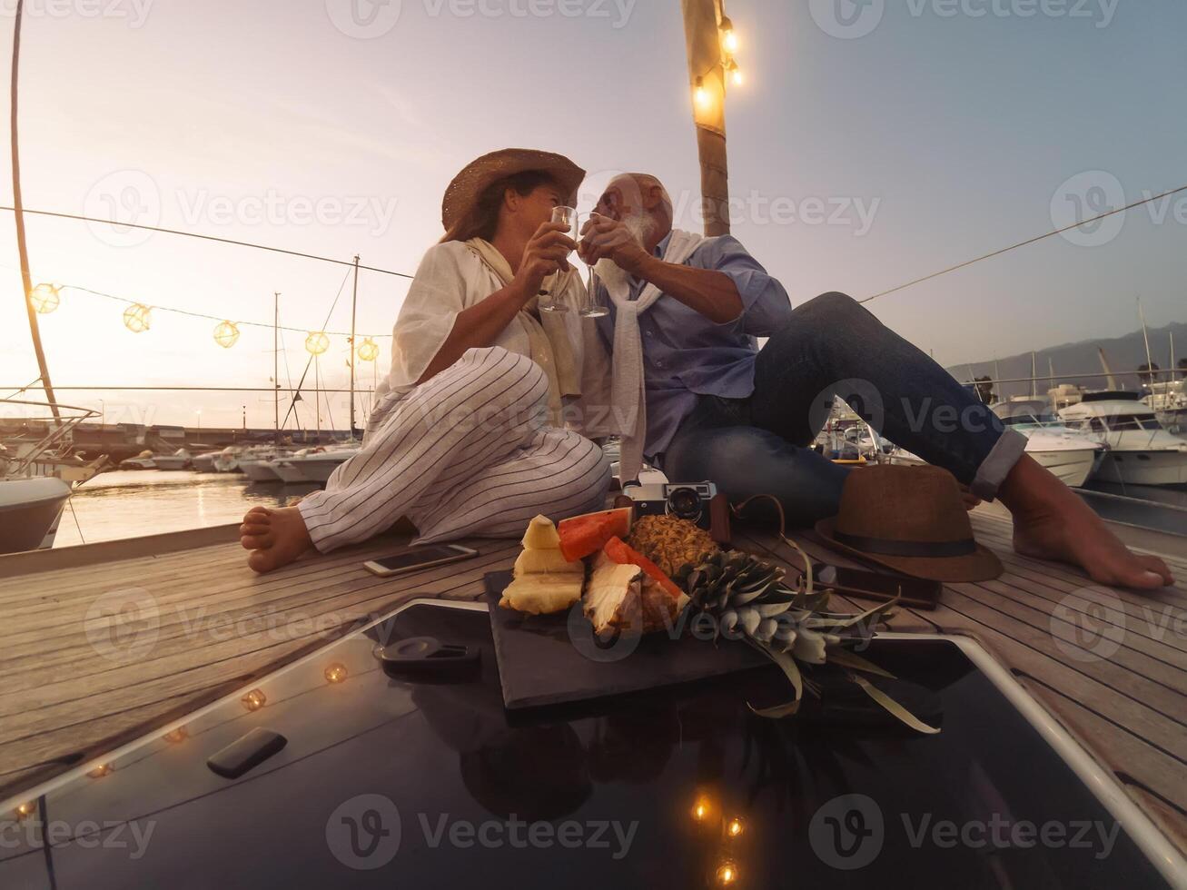 Senior couple toasting champagne on sailboat vacation - Happy mature people having fun celebrating wedding anniversary on boat trip - Love relationship and travel lifestyle concept photo