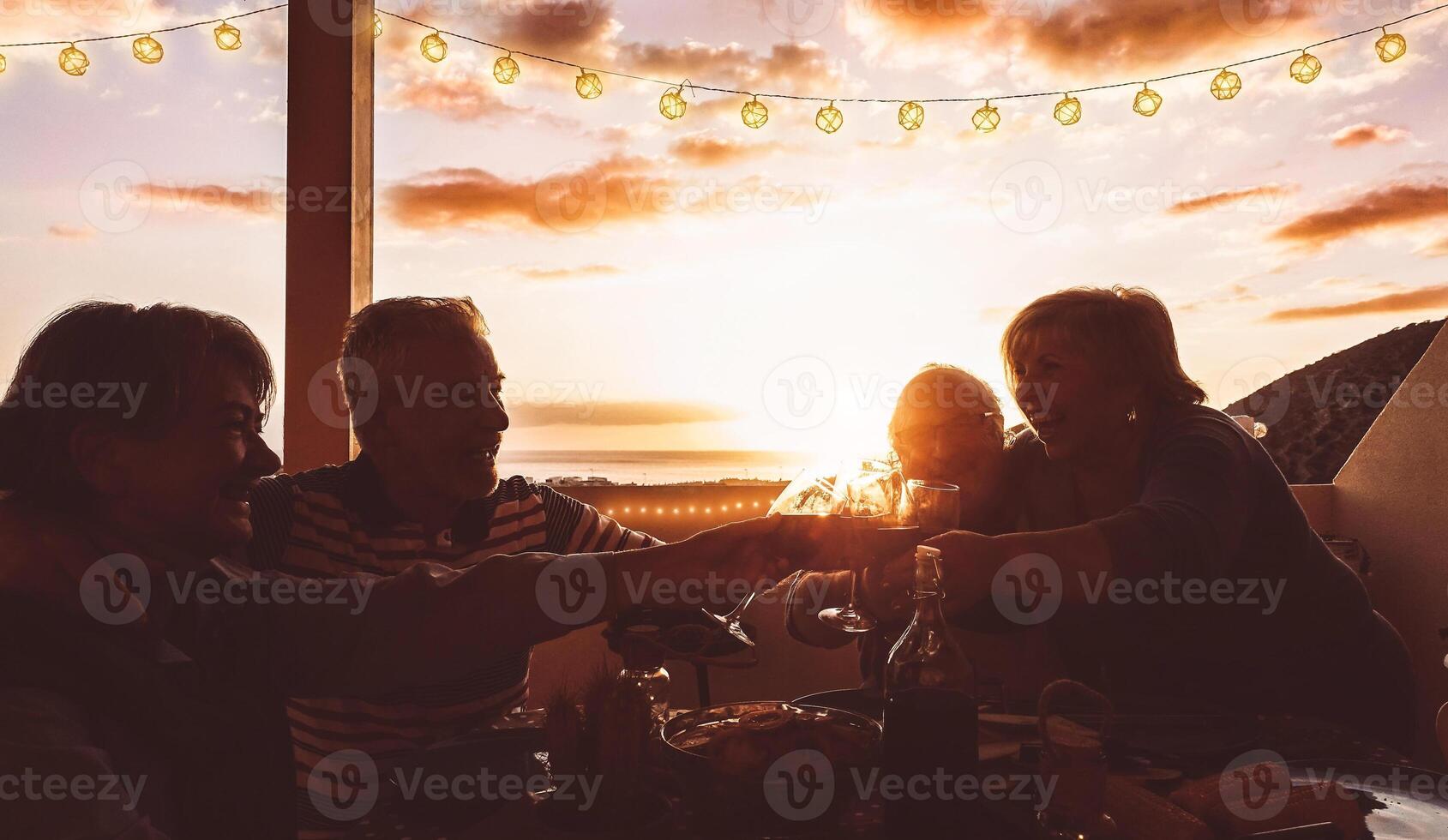 contento mayor amigos aplausos y tostado con rojo vino a terraza cena - maduro personas teniendo divertido comida juntos en techo a puesta de sol - amistad, comida y beber, mayor estilo de vida concepto foto