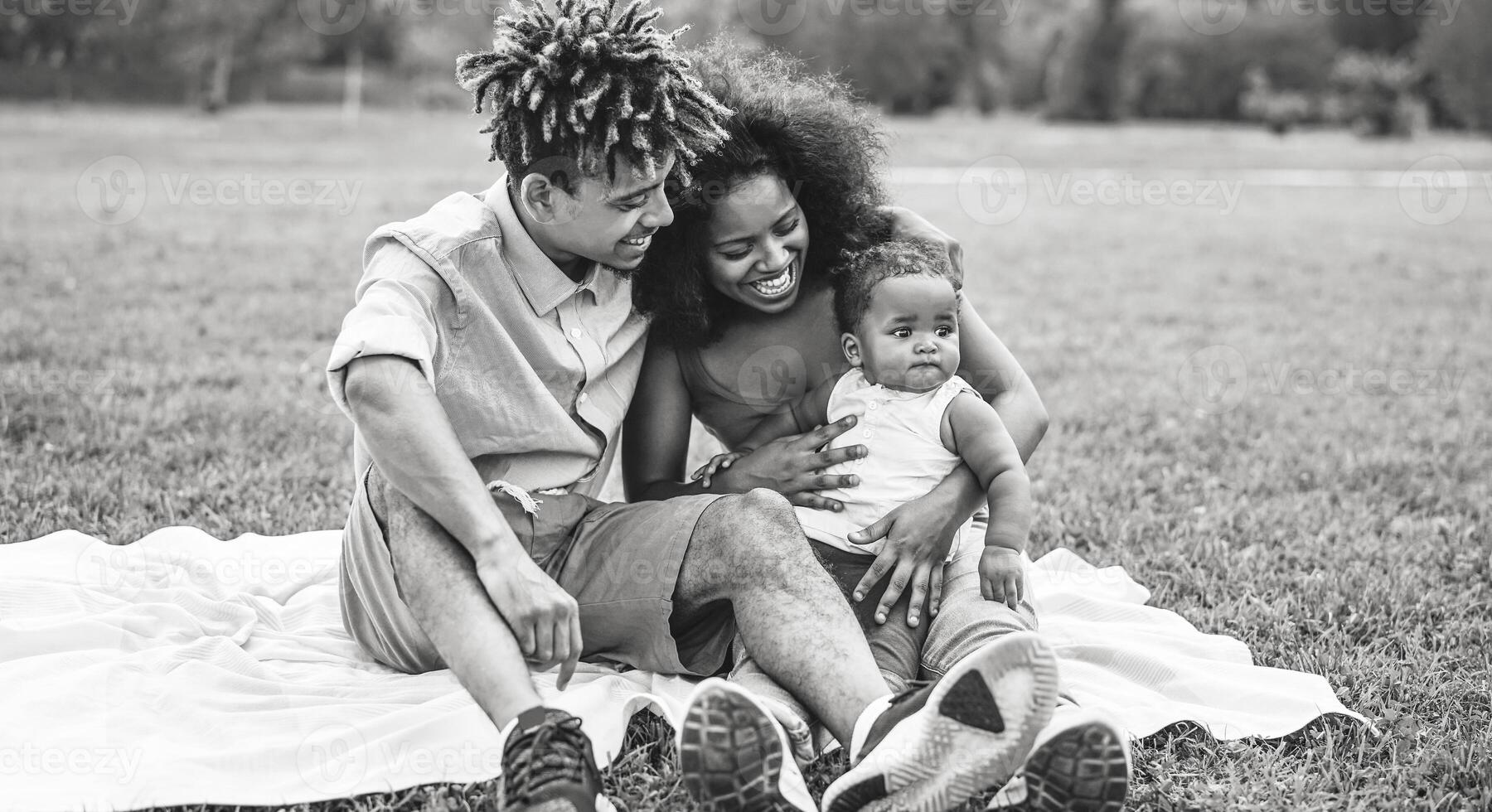 Happy African family having fun during the weekend in public park - Mother and father playing with their daughter outdoor - Love, parenthood and happiness concept - Black and white edited photo