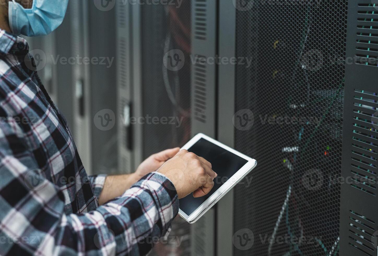 Male informatic engineer working inside server room database while wearing face mask during corona virus outbreak photo
