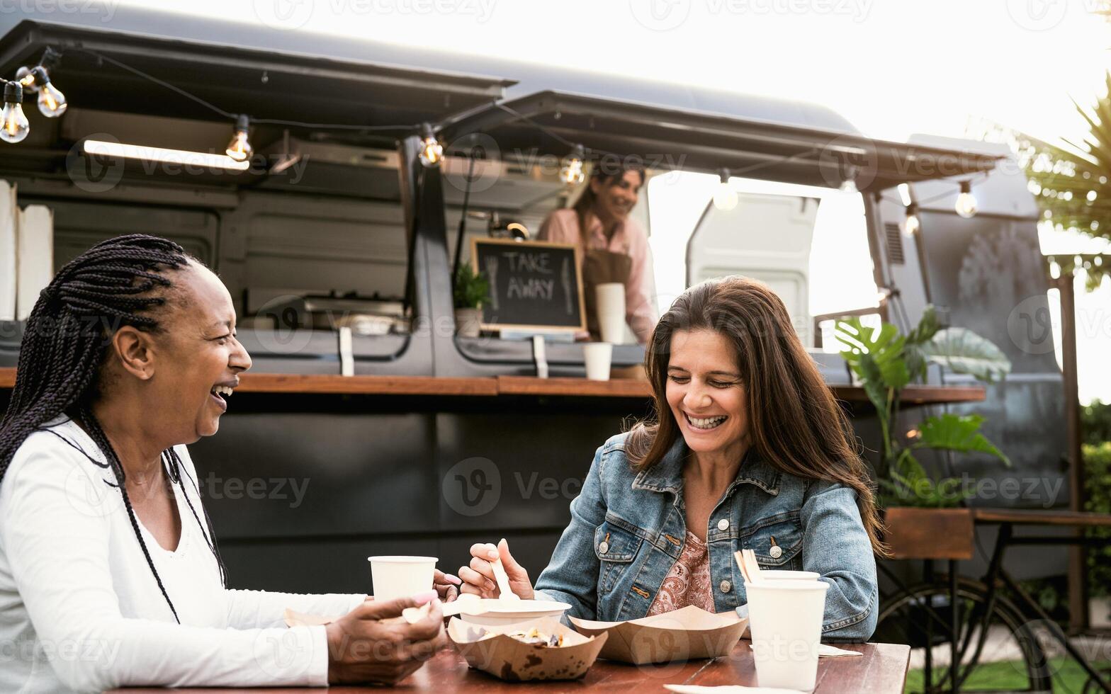 Happy multiracial senior friends having fun eating in a street food truck market photo