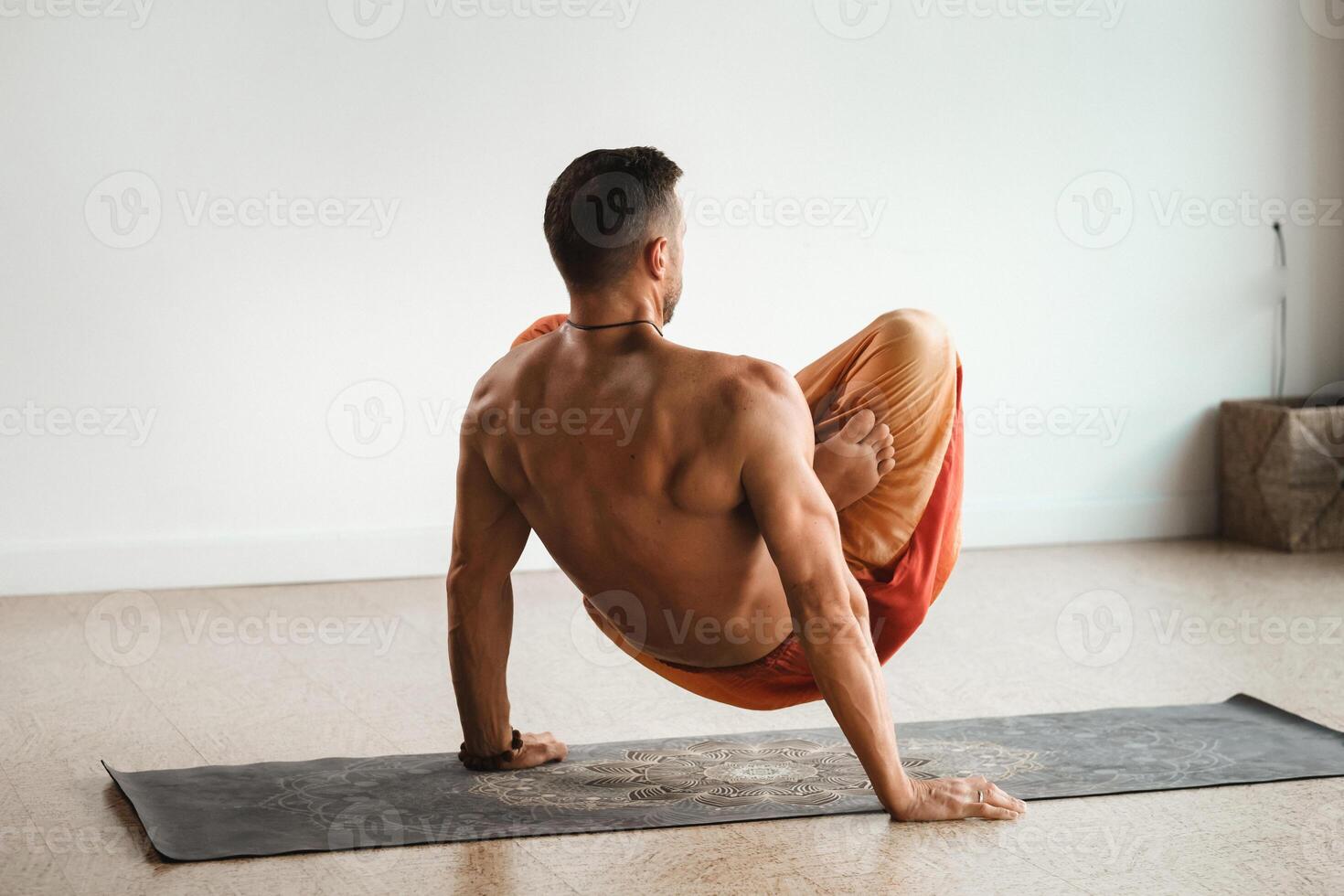 a man with a naked torso does yoga standing on his hands indoors. Fitness Trainer photo