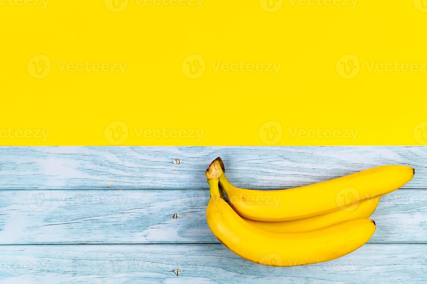 Yellow bananas lie on a blue wooden background and a yellow background photo