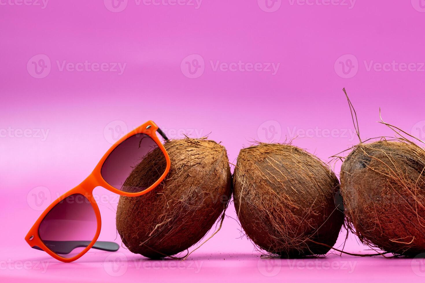 three whole coconuts and orange glasses on a pink background photo