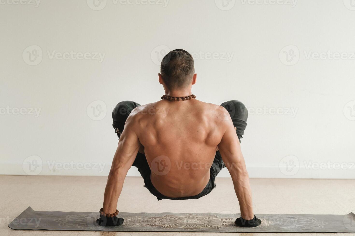 a man with a naked torso does yoga standing on his hands indoors. Fitness Trainer photo
