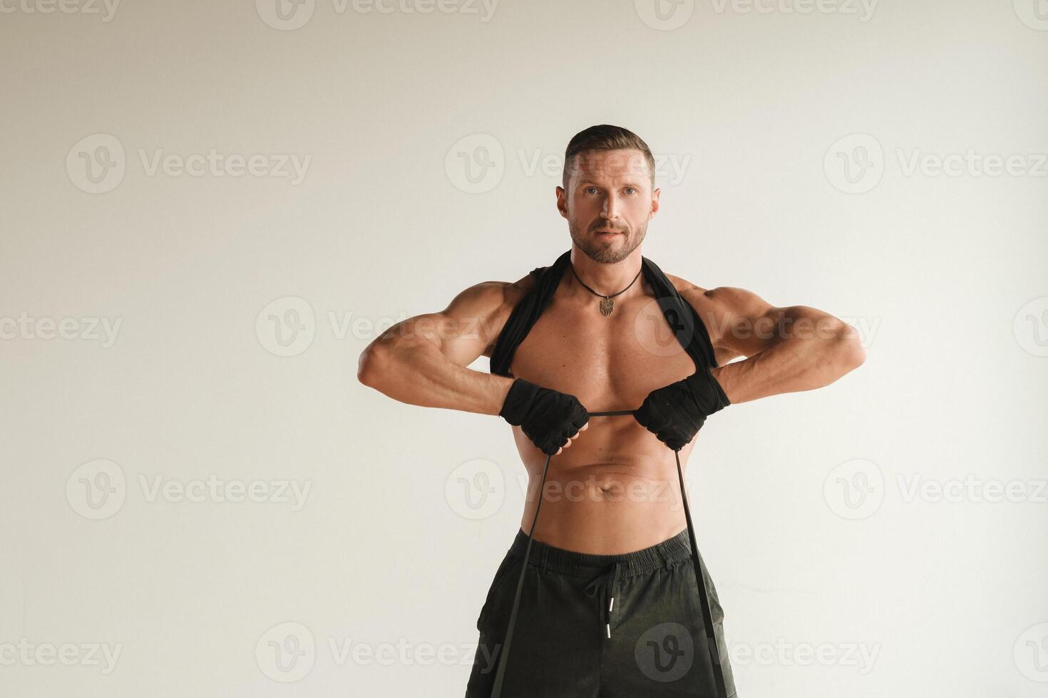 A man with a naked torso is engaged in strength fitness using a rubber loop indoors photo