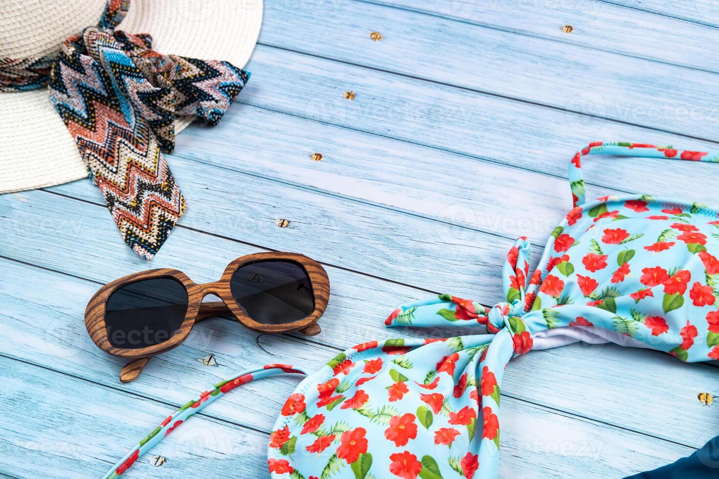 Top view of a straw white hat with glasses and a swimsuit, lying on a blue wooden background.Summer vacation concept photo