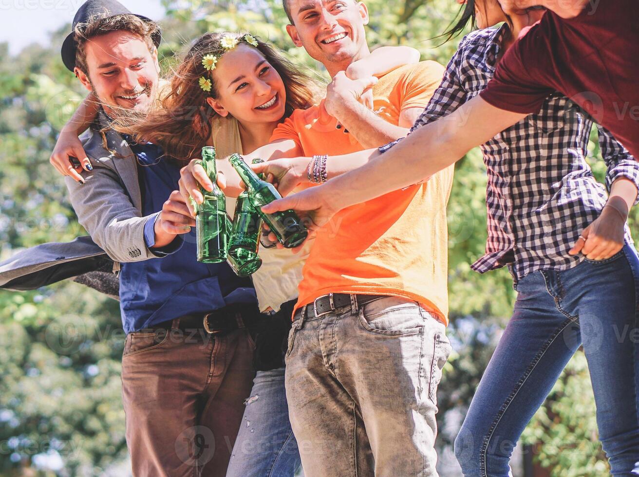 grupo de amigos aplausos y Bebiendo cervezas al aire libre - contento joven personas teniendo divertido tostado botellas de cerveza y riendo juntos - amistad, fiesta y juventud estilo de vida concepto foto