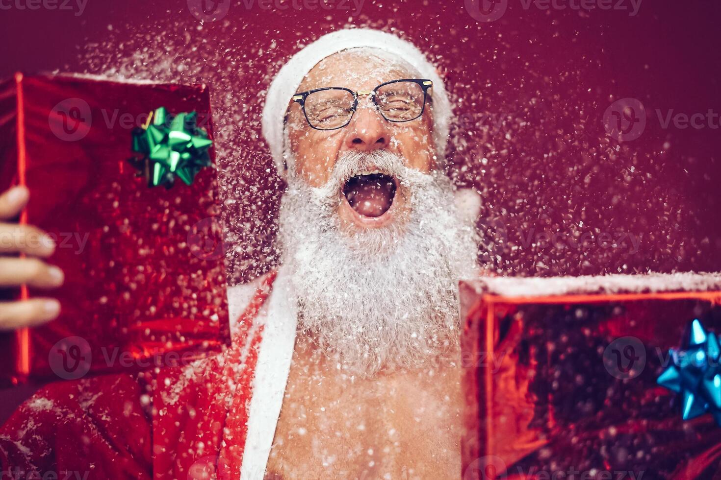 Happy crazy santa claus holding christmas box gifts - Hipster sanior man having fun laughing and wearing xmas winter costume - Concept of people doing funny celebration of x-mas holidays photo