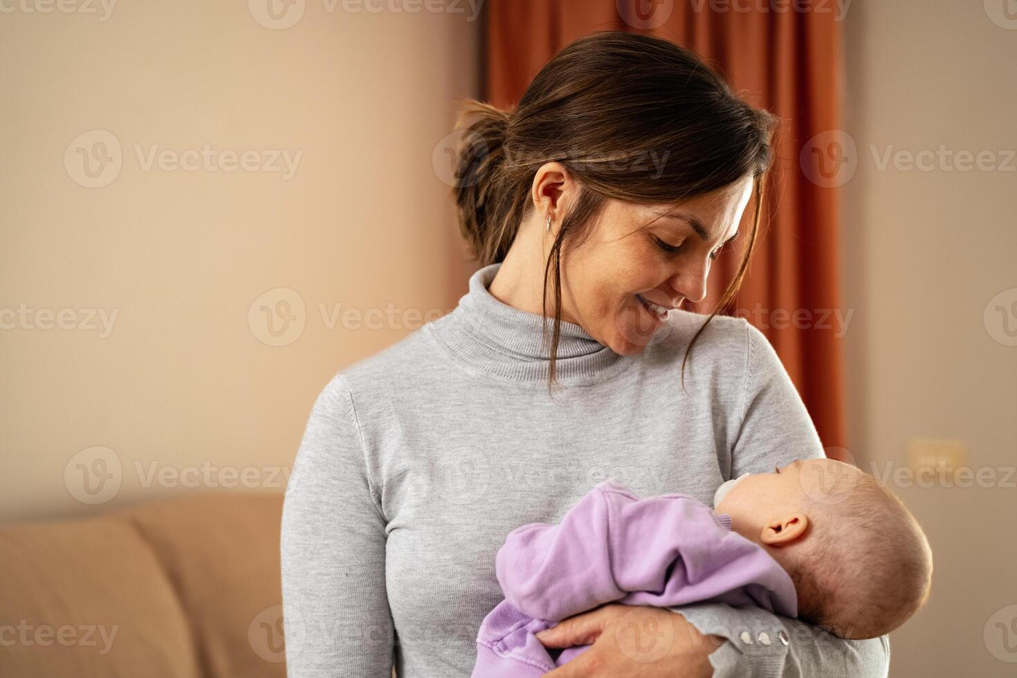 Happy mother taking care of her small baby sleeping in her arms at home - Concept family and motherhood photo